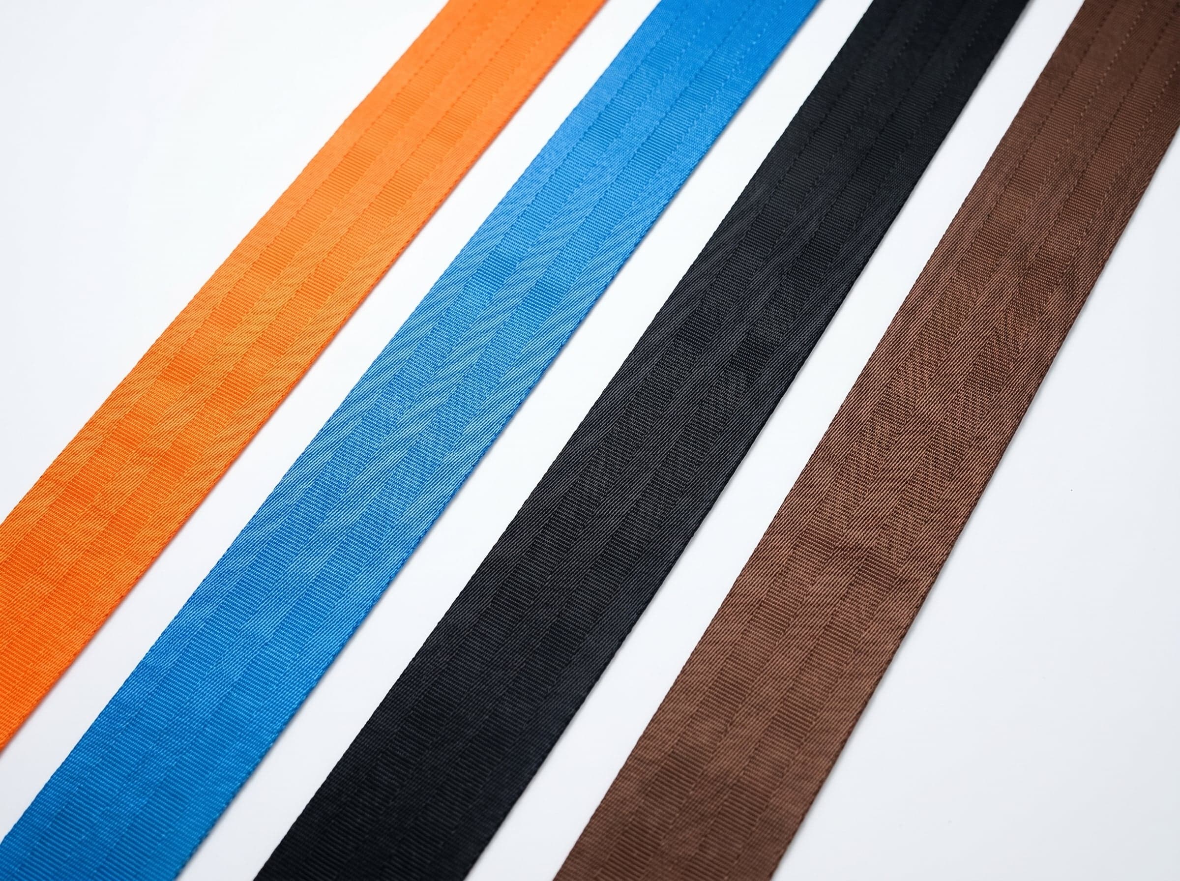 Orange, blue, black, and brown polyester webbing strips on a white studio surface