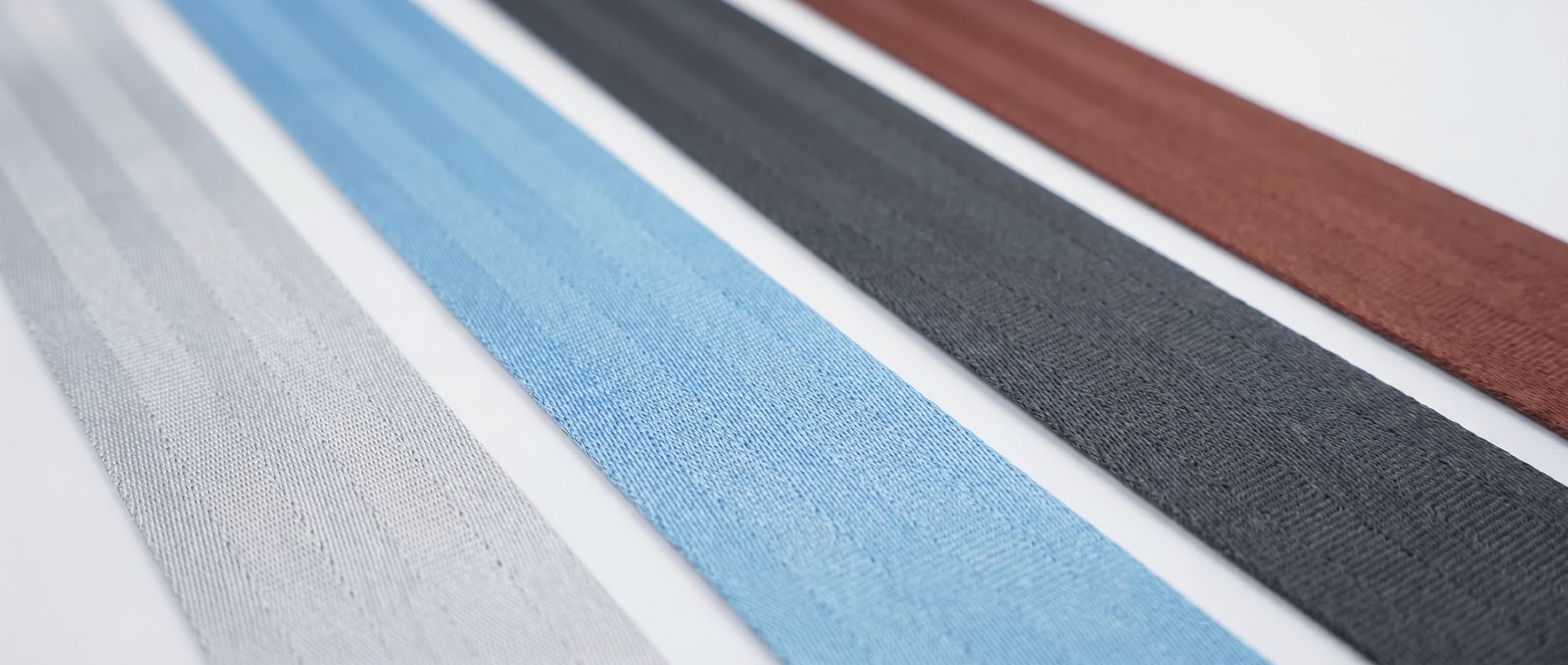 Close-up of gray, blue, black, and brown polyester webbing strips on a white surface